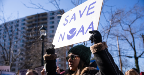A woman holding up a white sign that reads Save NOAA